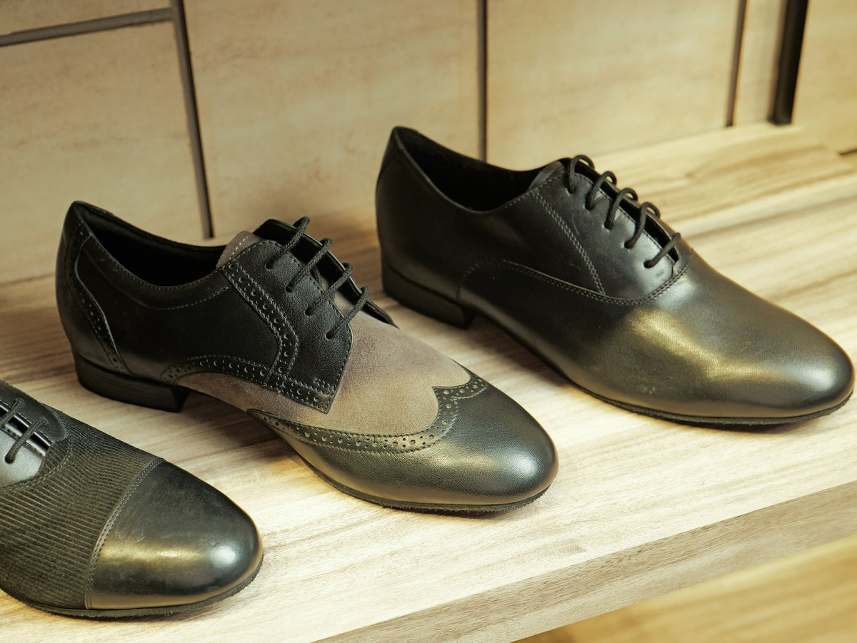Black leather and grey suede wingtip brogues on a showroom shelf