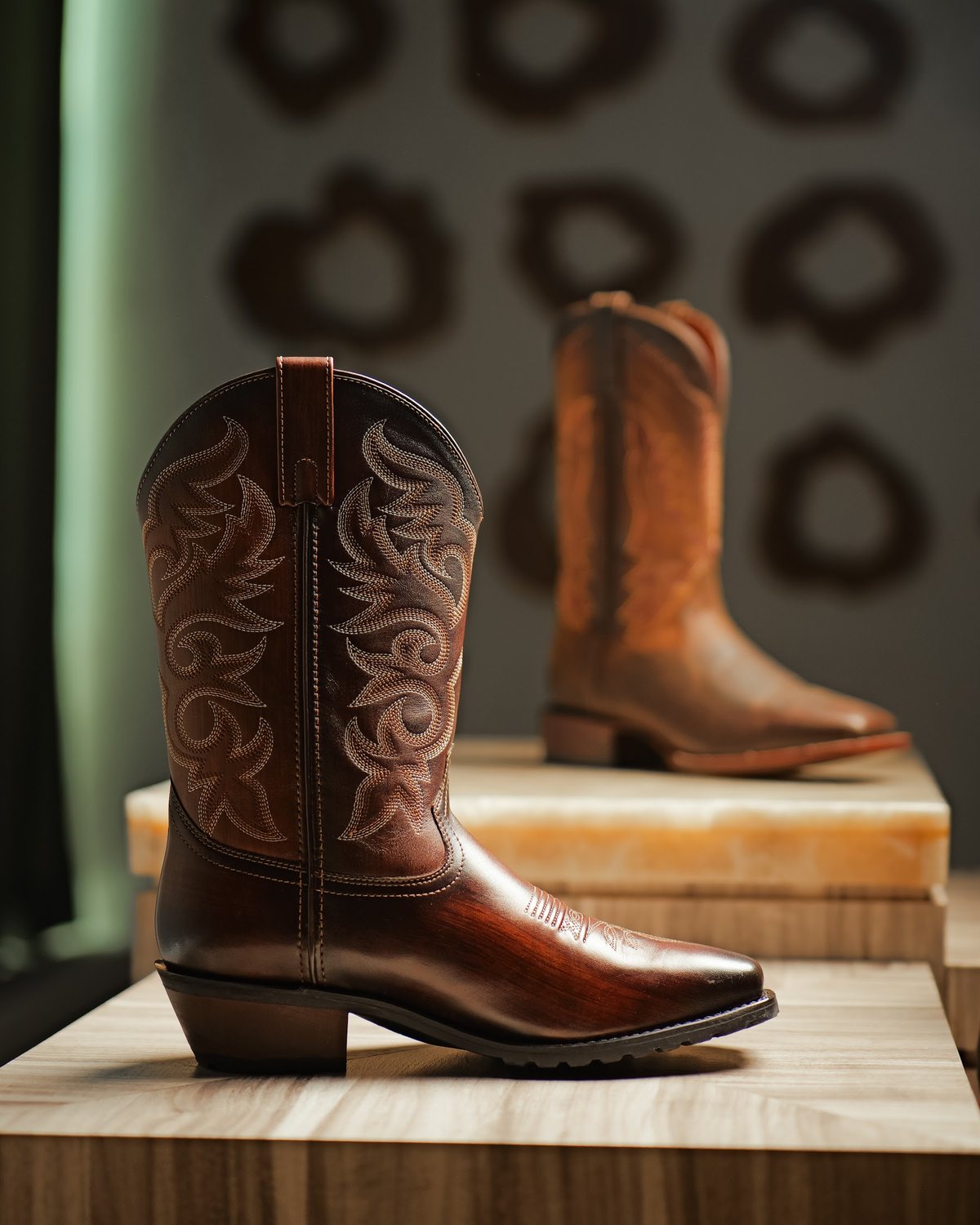 A brown cowboy boot with an embroidered shaft on a stone plinth