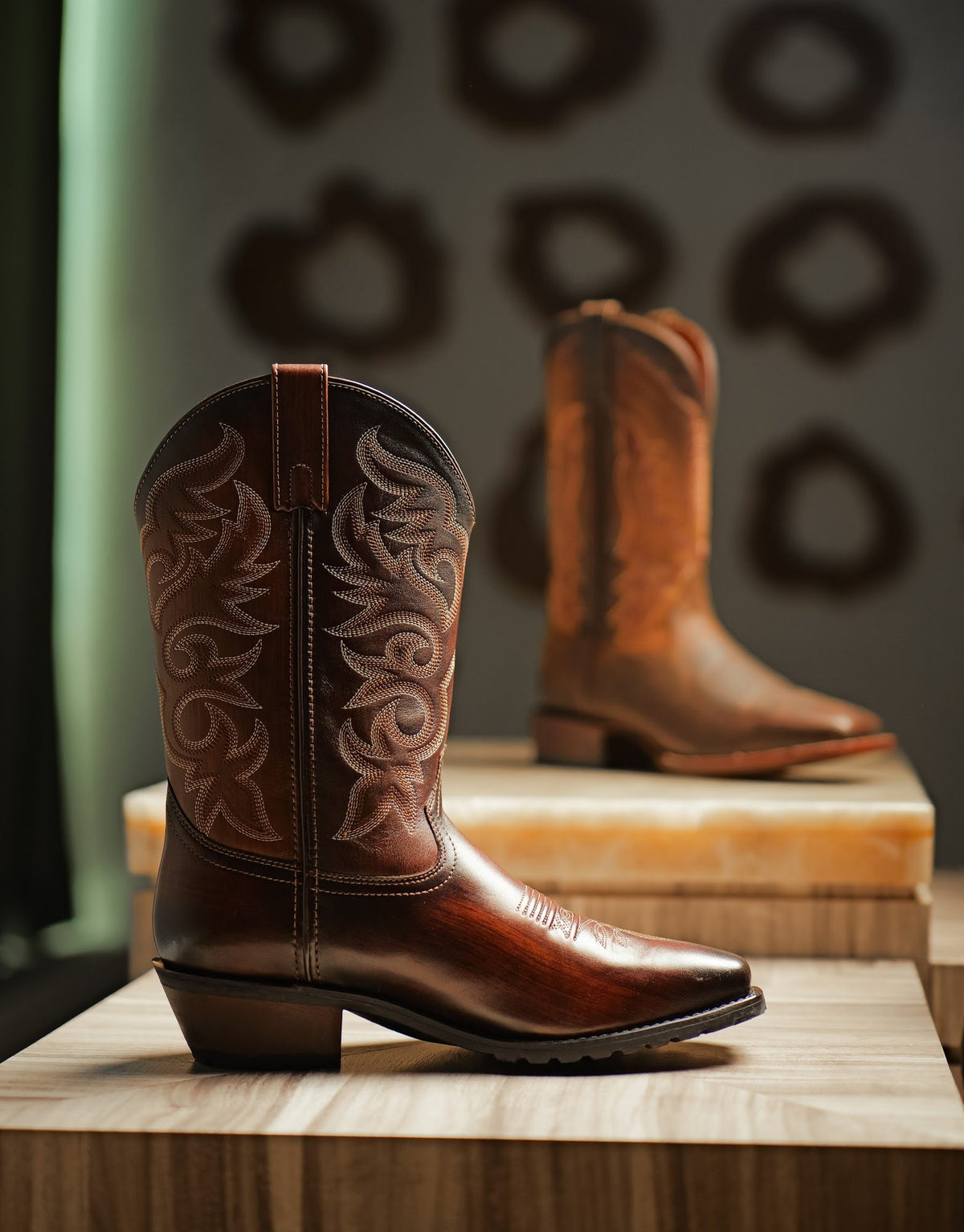 A burgundy men’s cowboy boot with an embroidered shaft, Goodyear welted, on a stone plinth