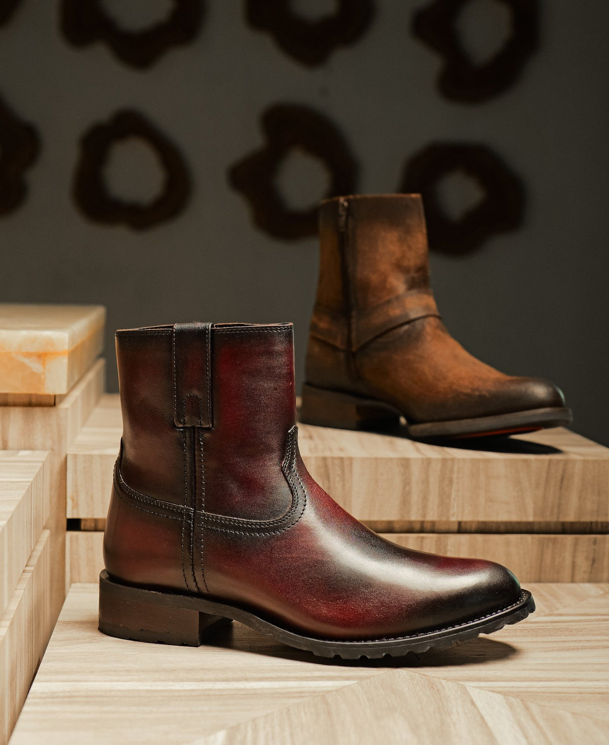 A burgundy pull-on utility boot with a brown boot behind it, on stone plinths