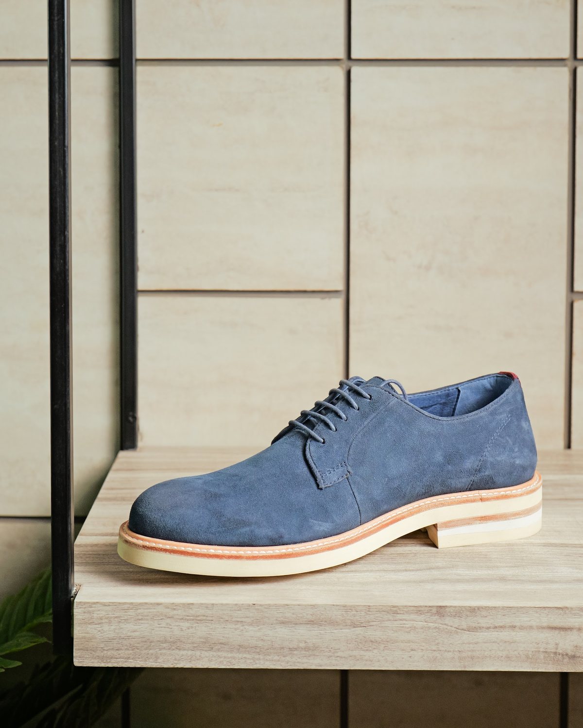 A navy suede men’s derby with a light sole on a showroom shelf