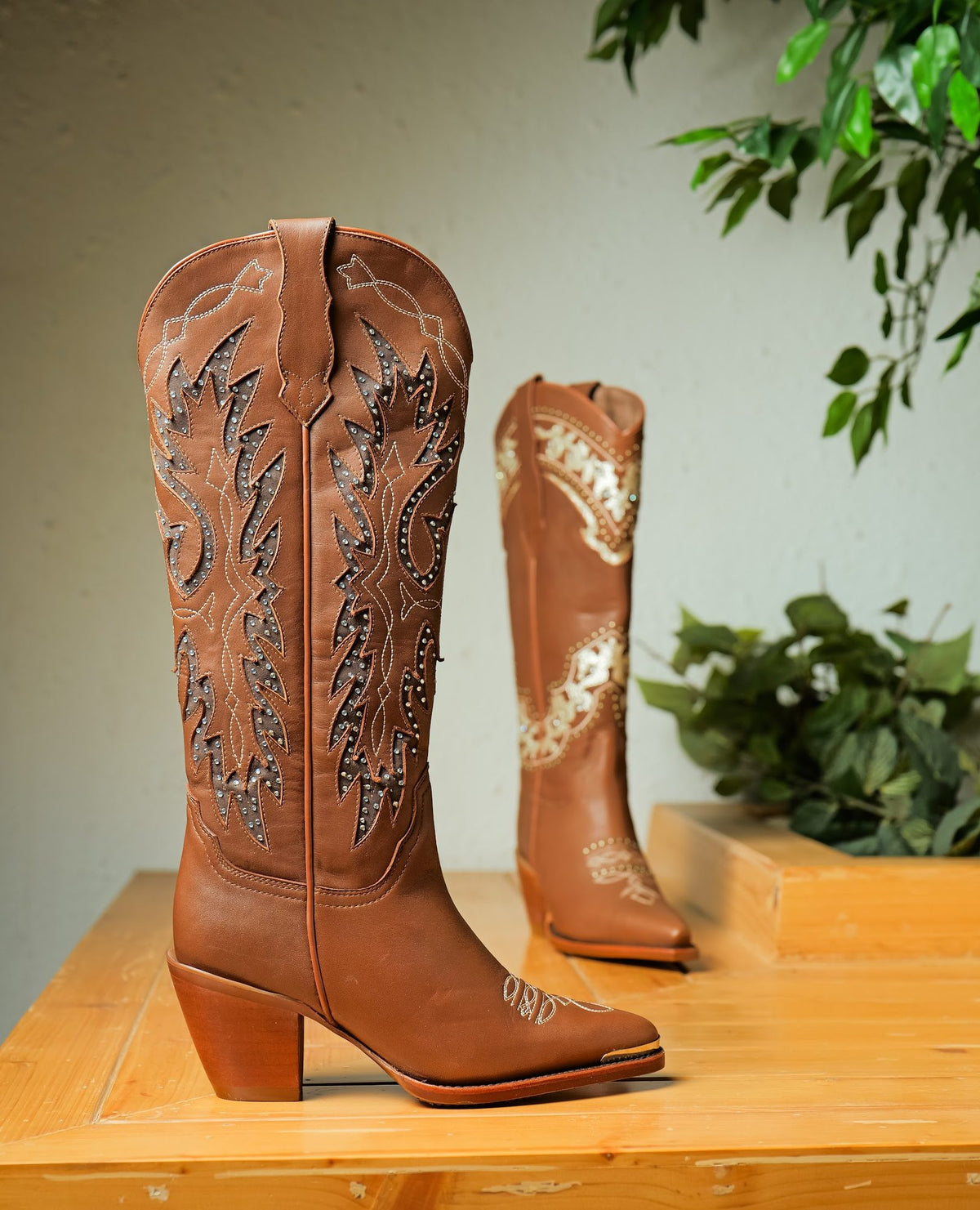 A tall cognac Western boot with studded, stitched shaft panels, beside a shorter boot