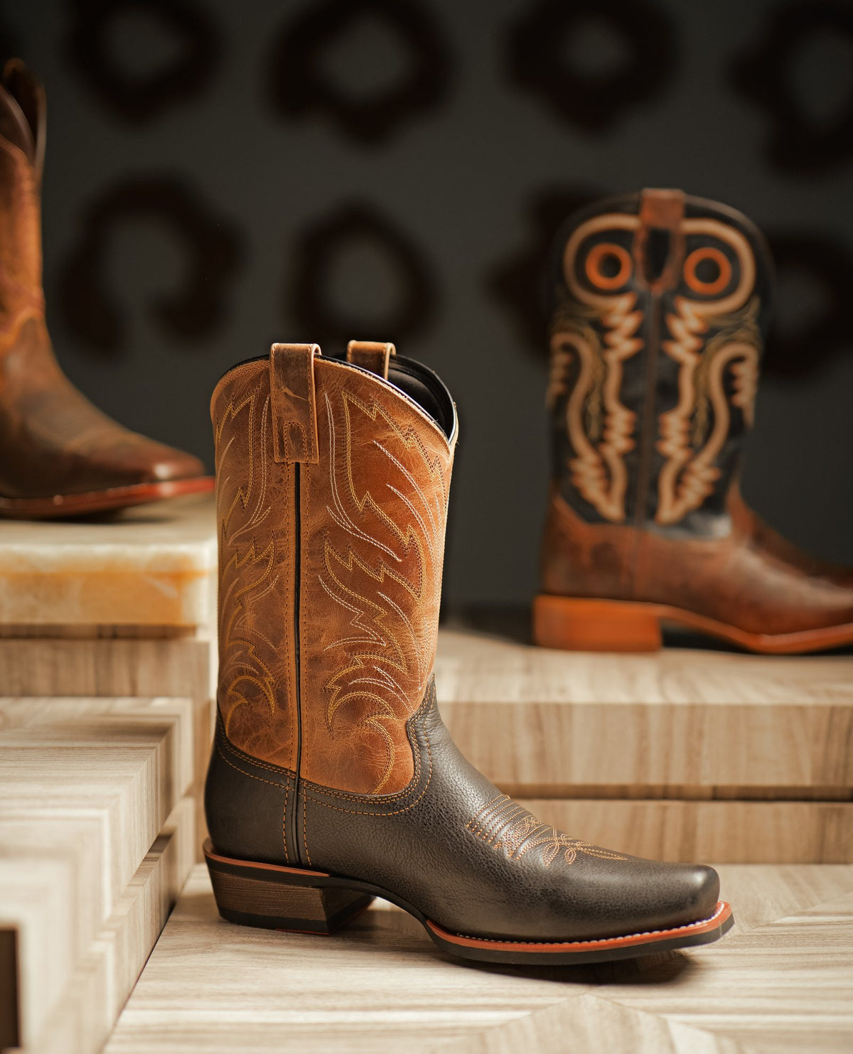 A tan cowboy boot with a stitched shaft on a stone plinth