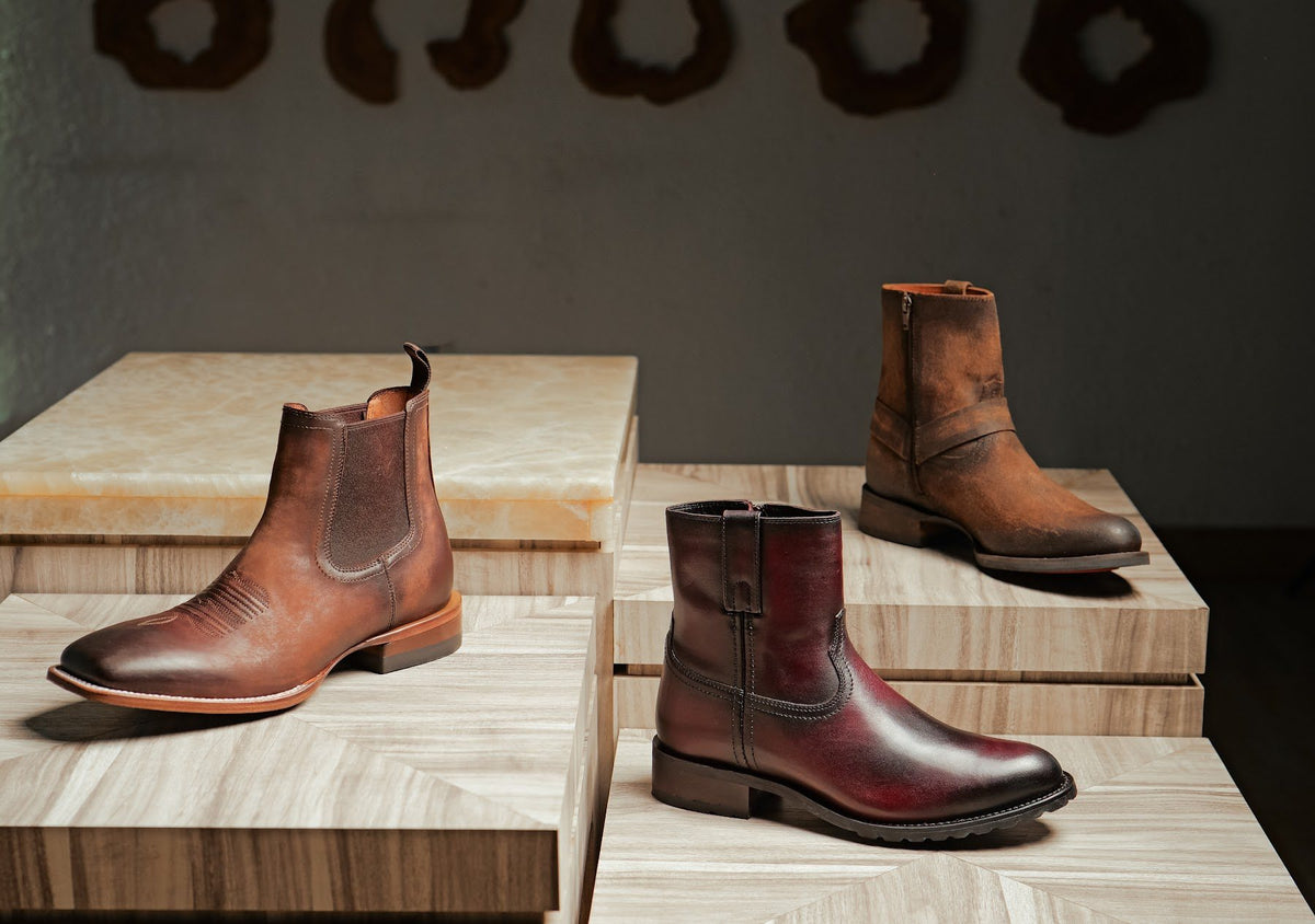 A tan Western Chelsea, a burgundy pull-on and a brown utility boot on stone plinths