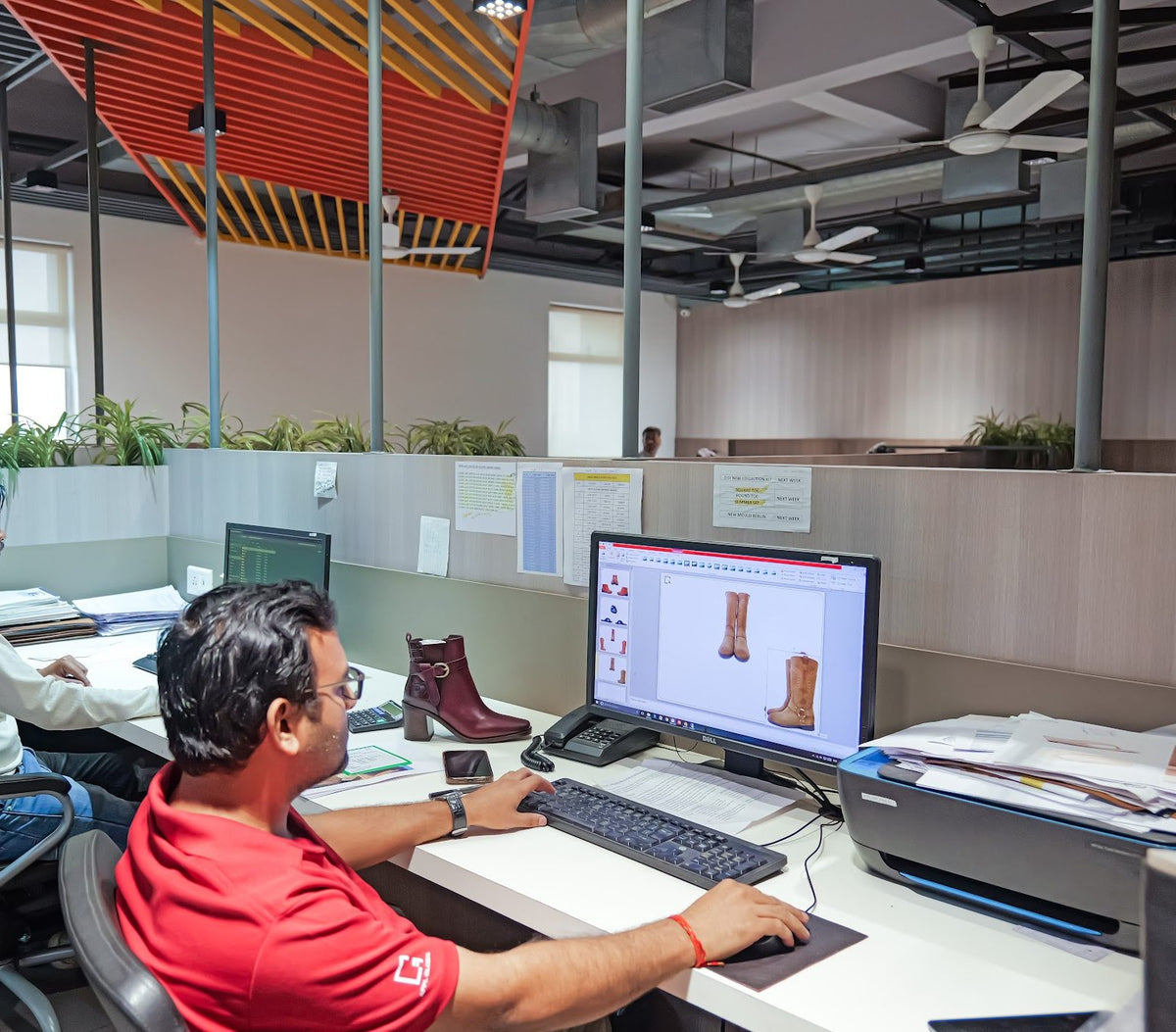 A designer developing boot styles on screen, with a sample on the desk