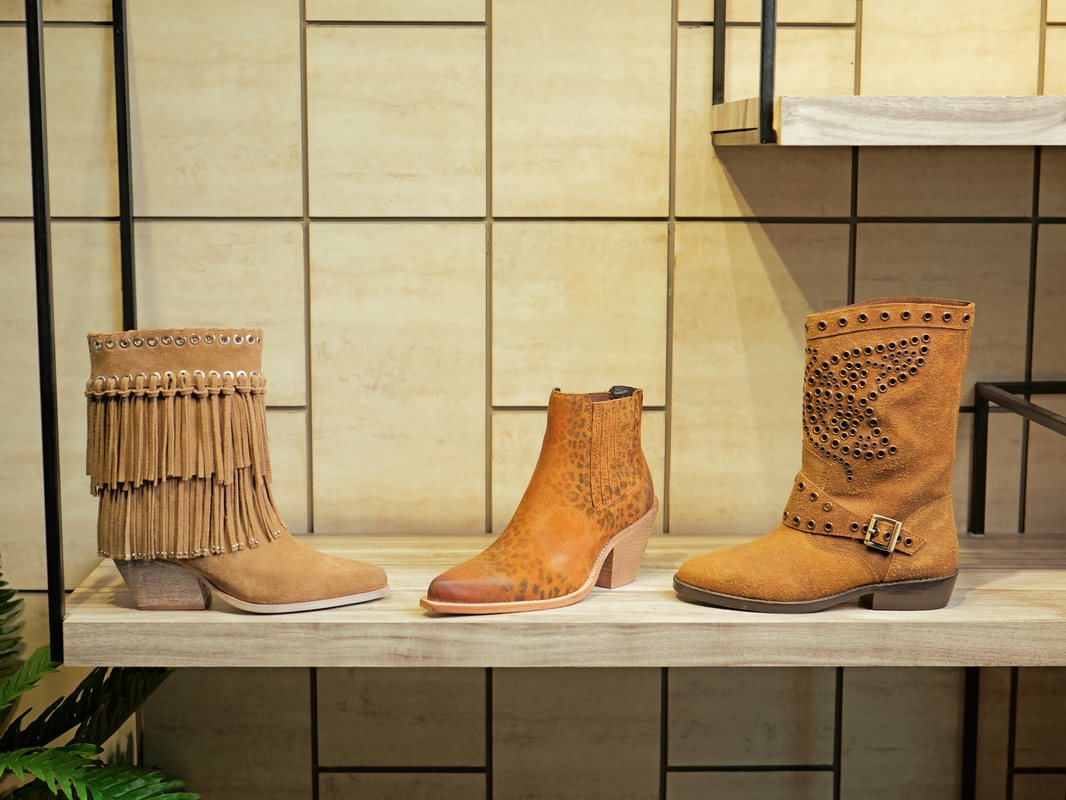 A fringed suede boot, a cognac ankle boot and a studded suede biker boot on a showroom shelf