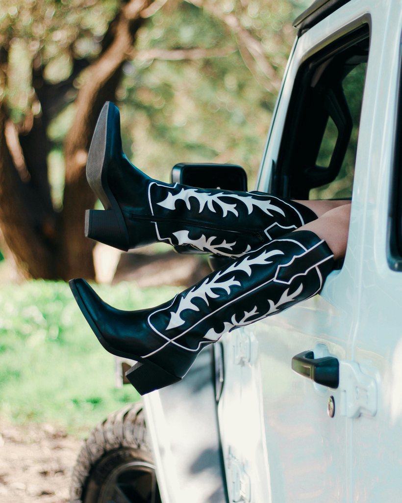 A pair of black Western boots with white inlay, resting on a car window