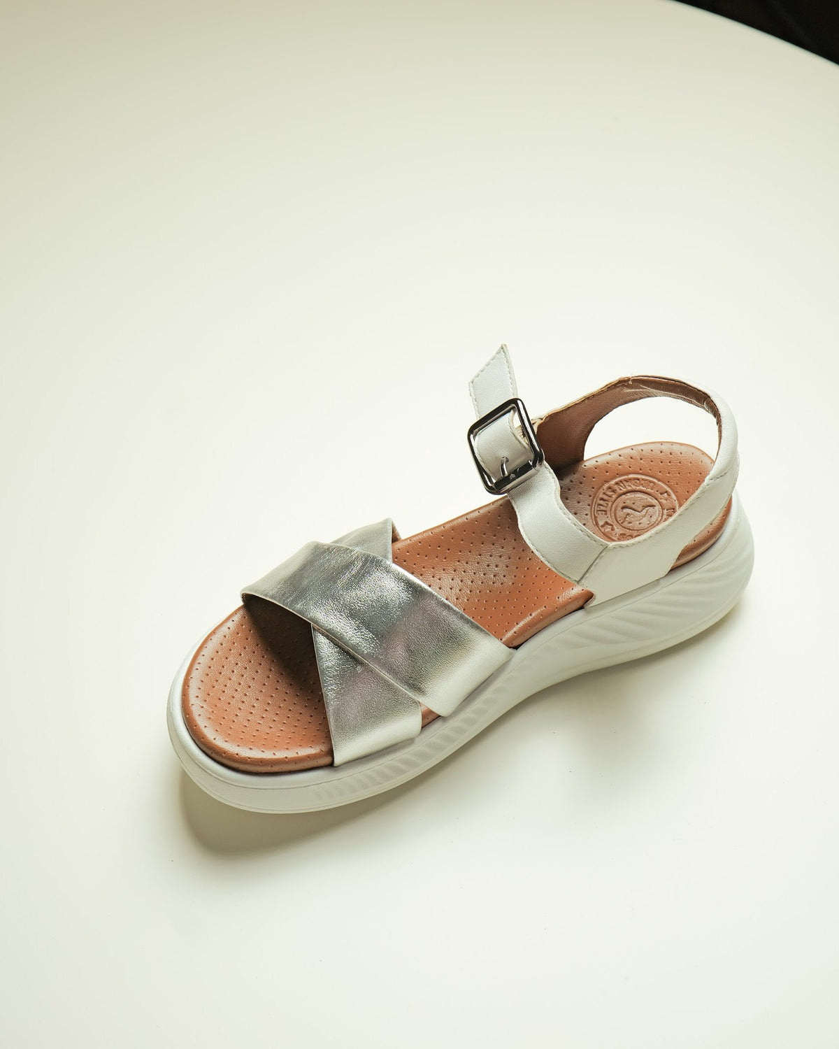 A silver leather crossover sandal with a buckled strap on a light platform sole