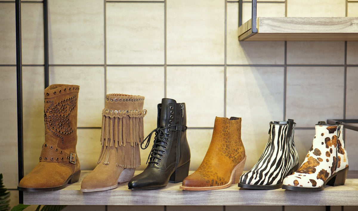 Six women’s fashion ankle and mid-calf boots on a showroom shelf