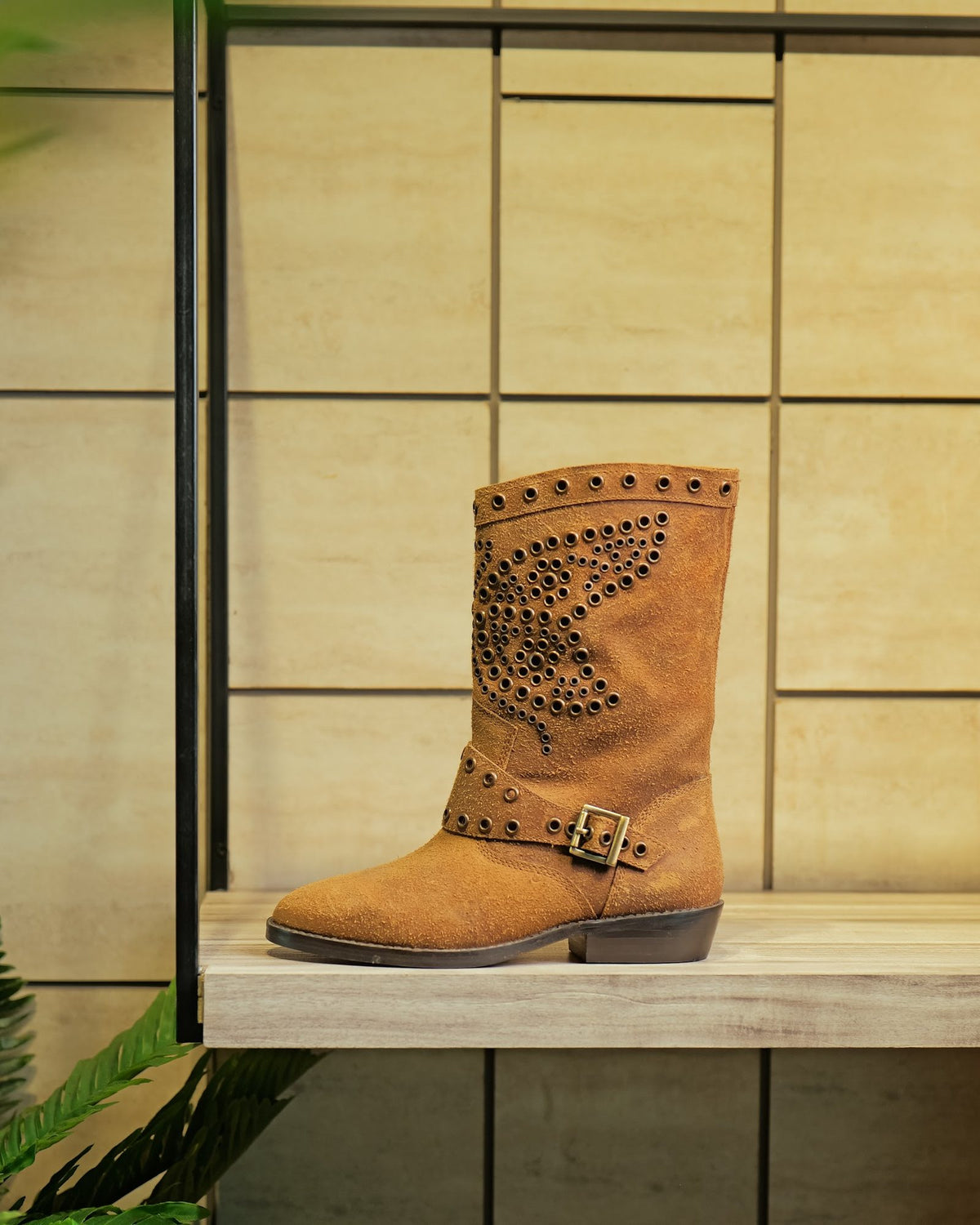 A studded suede boot with a buckle strap on a display shelf