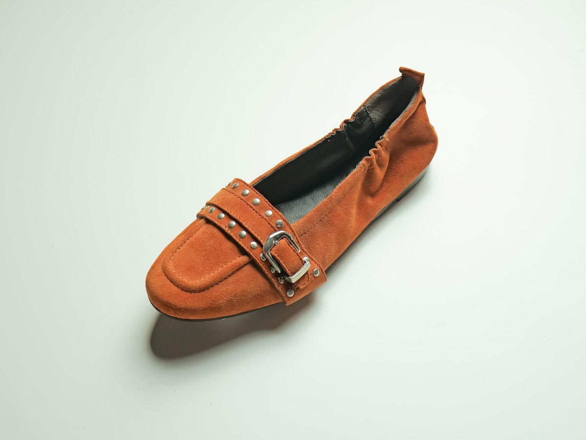 A suede loafer with a studded strap and buckle