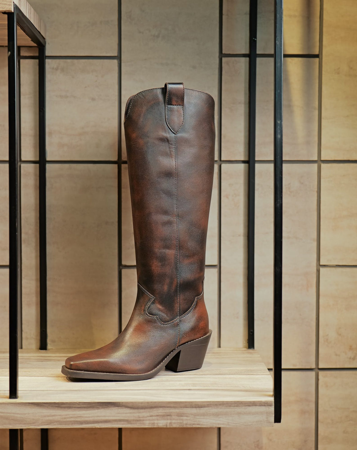 A tall brown leather boot on a display shelf