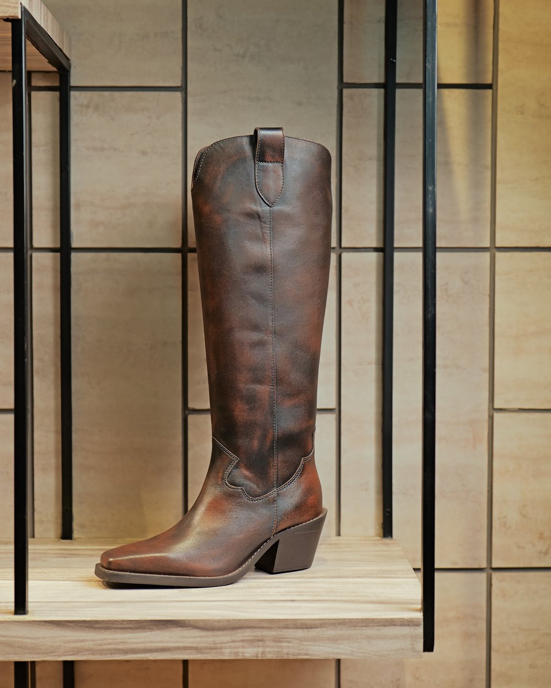 A tall brown leather fashion boot on a showroom shelf