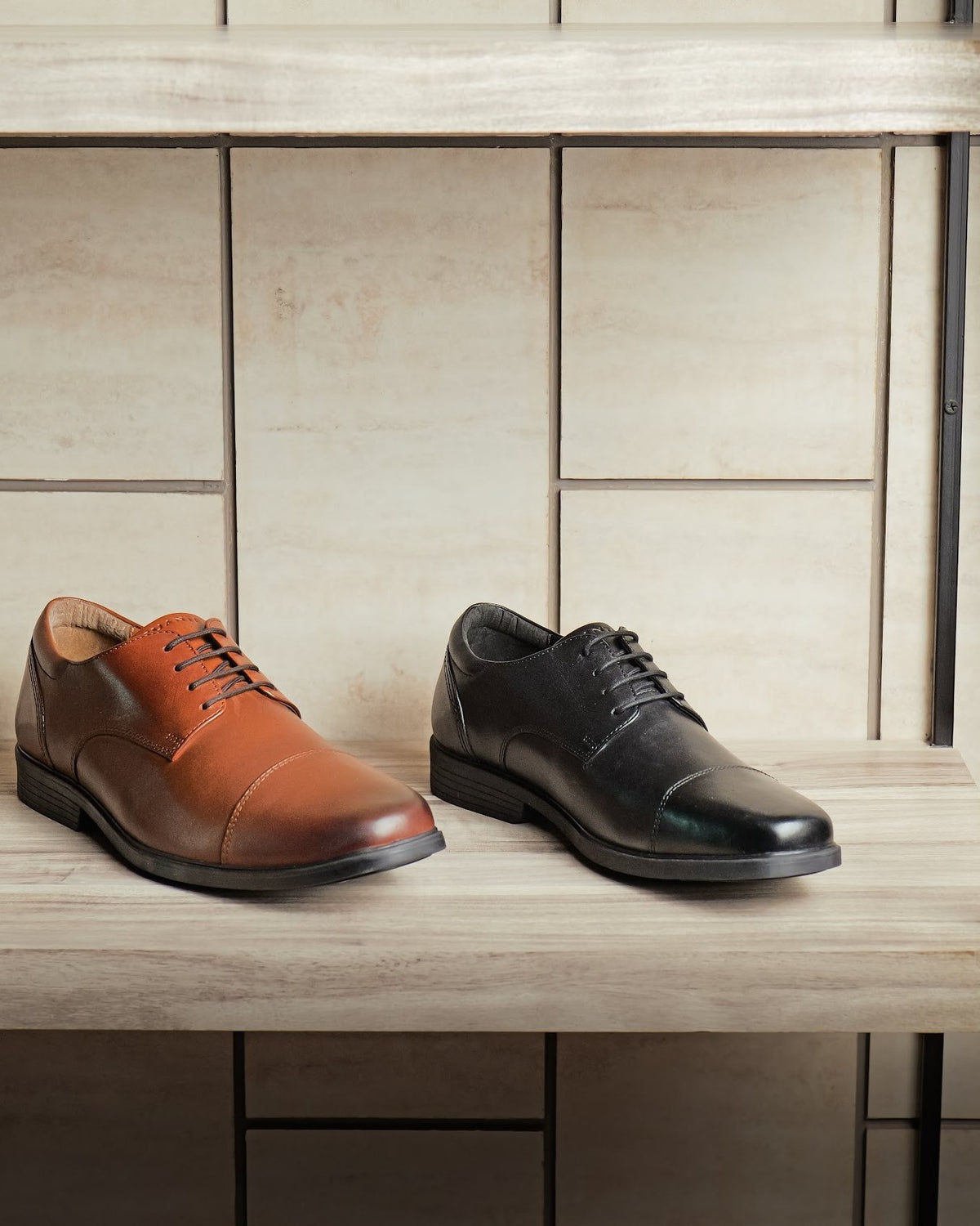 A tan and a black leather men’s cap-toe derby on a showroom shelf