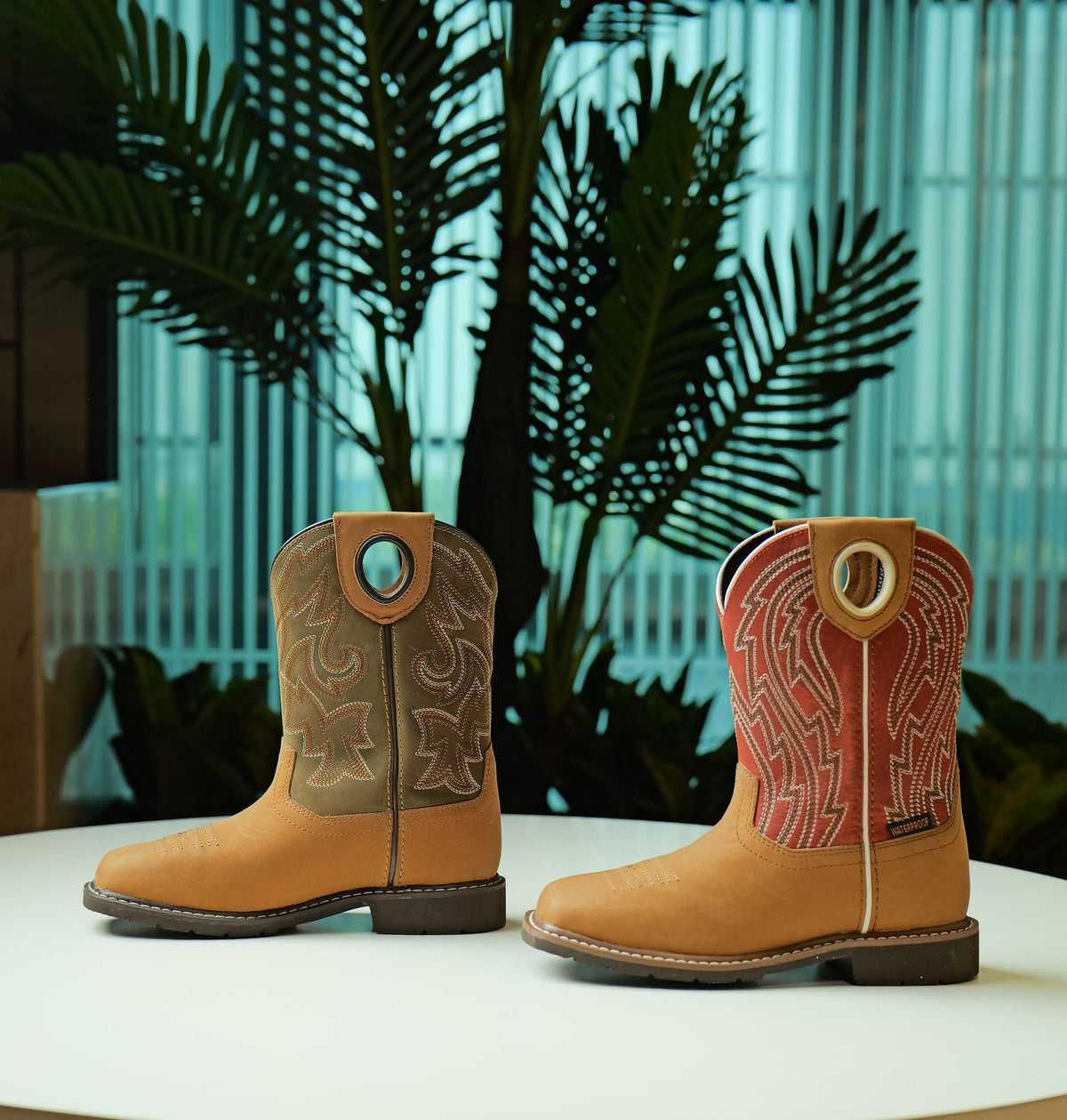 Two waterproof youth cowboy boots with embroidered shafts on a white table